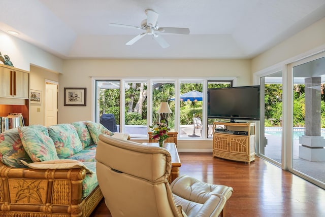 living area with wood finished floors, a raised ceiling, and ceiling fan