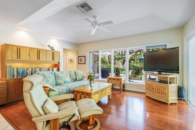 living area featuring a raised ceiling, ceiling fan, visible vents, and wood finished floors