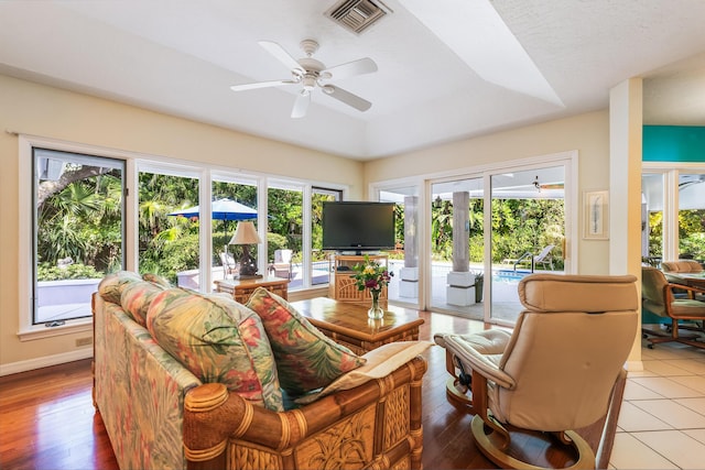 living area with wood finished floors, visible vents, baseboards, a raised ceiling, and ceiling fan