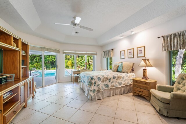bedroom with a ceiling fan, a tray ceiling, light tile patterned flooring, and access to exterior