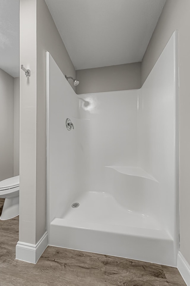 full bathroom with toilet, a shower, wood finished floors, and baseboards