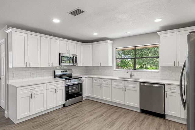 kitchen featuring stainless steel appliances, a sink, recessed lighting, light wood-type flooring, and light countertops