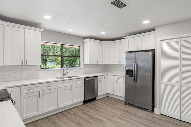 kitchen featuring stainless steel appliances, a sink, light countertops, white cabinets, and recessed lighting