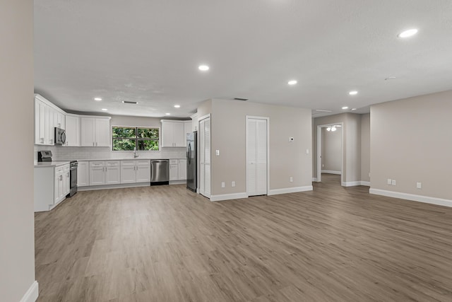 kitchen with appliances with stainless steel finishes, open floor plan, light wood-style flooring, baseboards, and recessed lighting
