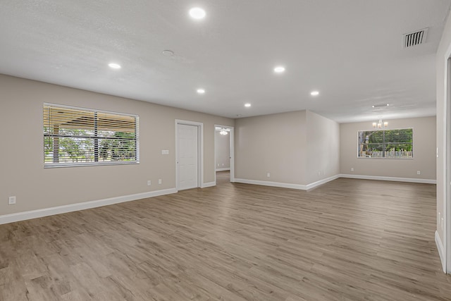 empty room with light wood-type flooring, recessed lighting, baseboards, and a chandelier
