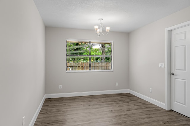 empty room with a chandelier, wood finished floors, baseboards, and a textured ceiling
