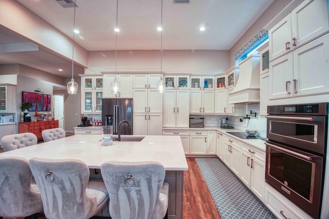 kitchen featuring multiple ovens, high quality fridge, a sink, black electric stovetop, and a large island with sink