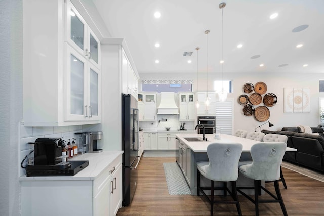 kitchen with premium range hood, black fridge, tasteful backsplash, dark wood finished floors, and a breakfast bar area