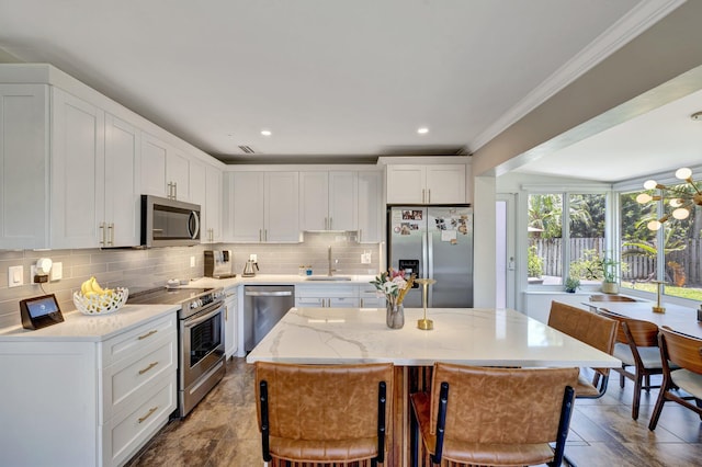 kitchen with a sink, crown molding, decorative backsplash, white cabinets, and appliances with stainless steel finishes