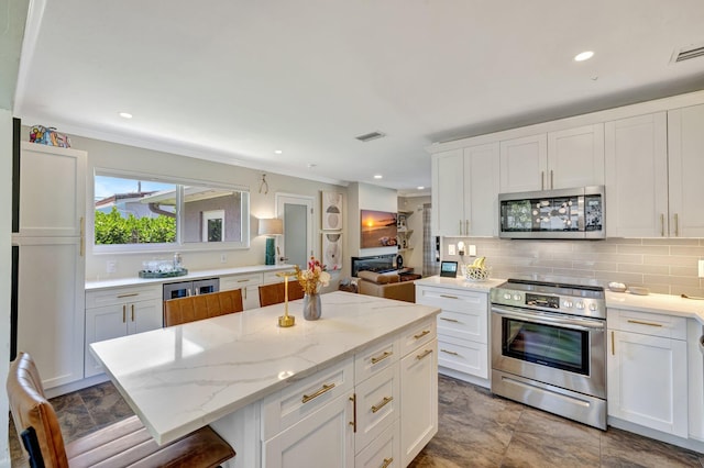 kitchen with light stone countertops, a center island, white cabinets, stainless steel appliances, and tasteful backsplash