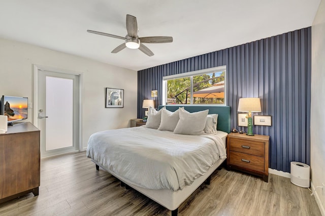 bedroom featuring an accent wall, light wood finished floors, ceiling fan, baseboards, and wallpapered walls