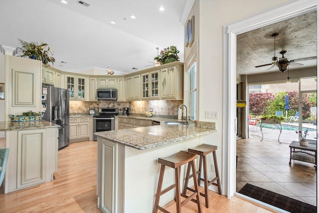kitchen featuring a ceiling fan, a sink, cream cabinetry, a peninsula, and appliances with stainless steel finishes