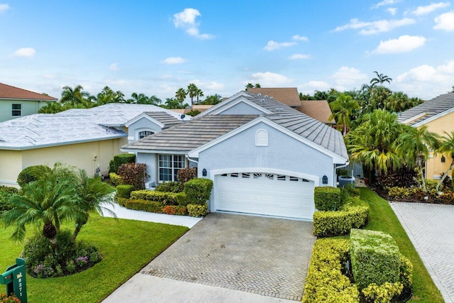 traditional-style home with an attached garage, stucco siding, a front lawn, and decorative driveway