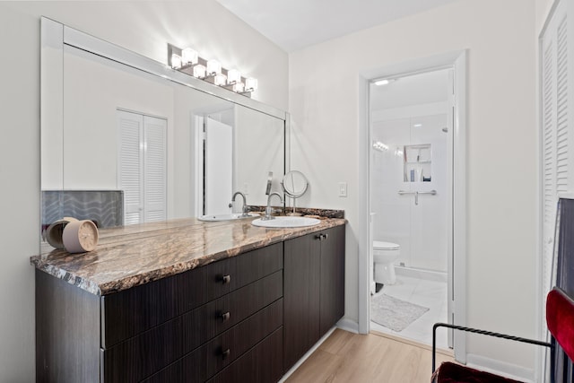 bathroom featuring toilet, a closet, wood finished floors, vanity, and baseboards