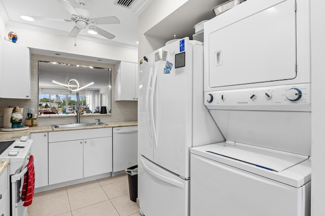 laundry area featuring stacked washer and clothes dryer, ceiling fan with notable chandelier, a sink, laundry area, and light tile patterned flooring