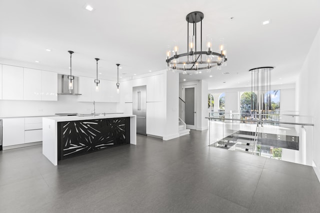 kitchen with modern cabinets, wall chimney range hood, a large island with sink, white cabinets, and a chandelier