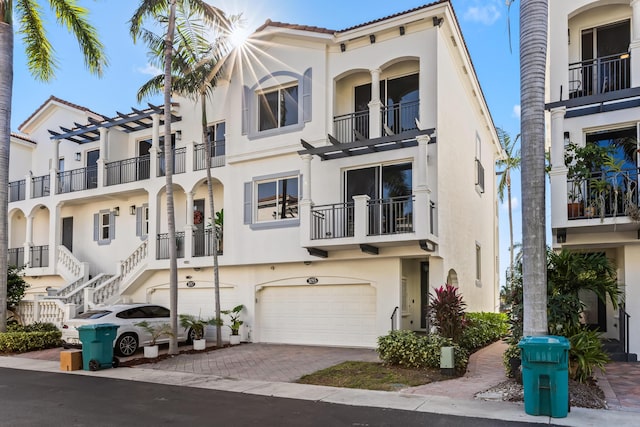 view of property featuring stucco siding, an attached garage, decorative driveway, and a balcony