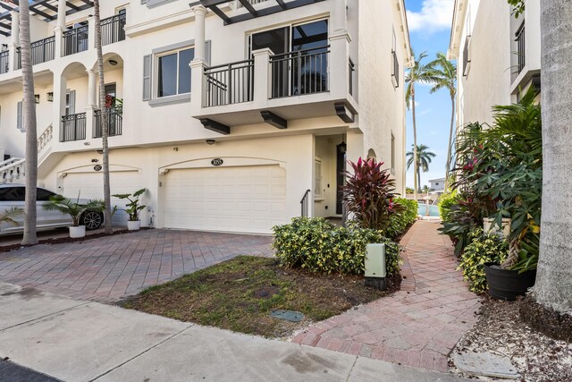 view of front of property featuring stucco siding, a garage, decorative driveway, and a balcony