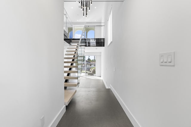 hall featuring baseboards, a towering ceiling, and a chandelier