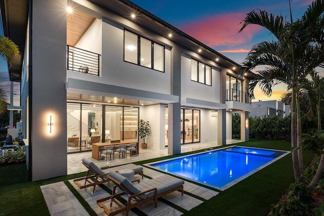 1445 NE 5th Ave, Boca Raton, FL 33432 - back of house at dusk featuring a balcony, stucco siding, a patio area, and an outdoor pool