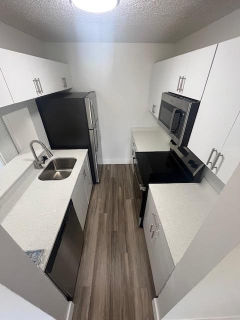 kitchen with a sink, light countertops, appliances with stainless steel finishes, dark wood-style floors, and a textured ceiling