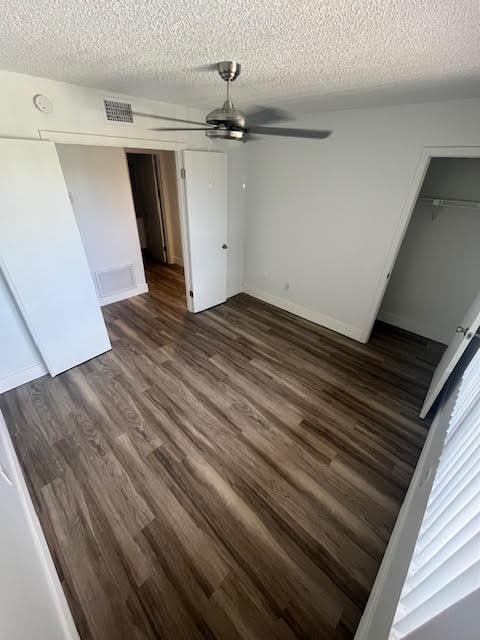 unfurnished bedroom with dark wood-style floors, a textured ceiling, a closet, baseboards, and ceiling fan