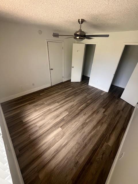unfurnished bedroom with a textured ceiling, baseboards, dark wood finished floors, ceiling fan, and a closet
