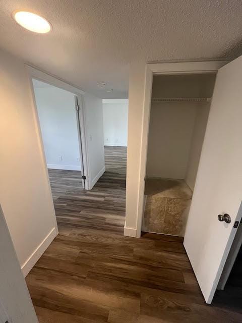 corridor featuring wood finished floors, a textured ceiling, and baseboards