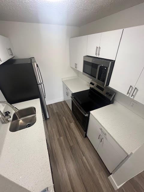 kitchen featuring stainless steel appliances, a sink, dark wood-type flooring, light countertops, and white cabinets