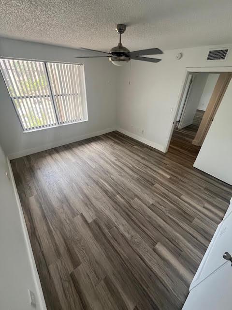 unfurnished room with ceiling fan, wood finished floors, a textured ceiling, and baseboards