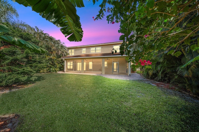 back of house at dusk with a lawn, a patio area, stucco siding, and ceiling fan