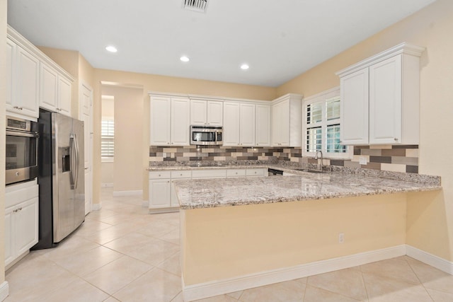 kitchen featuring a sink, a peninsula, stainless steel appliances, tasteful backsplash, and baseboards
