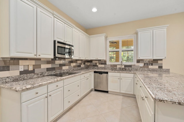 kitchen with a sink, stainless steel appliances, white cabinetry, light tile patterned floors, and light stone countertops