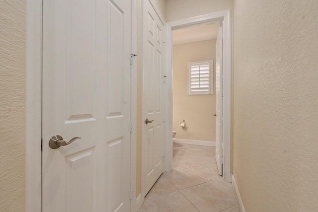corridor with a textured wall, baseboards, and light tile patterned floors