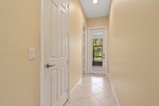 hallway with light tile patterned floors, baseboards, and a textured wall