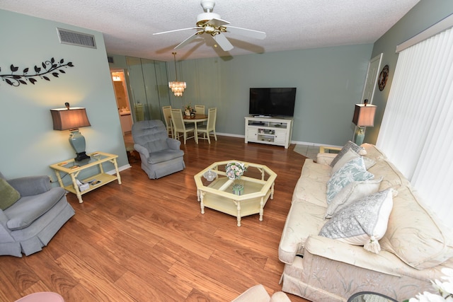living room featuring wood finished floors, ceiling fan with notable chandelier, a textured ceiling, visible vents, and baseboards