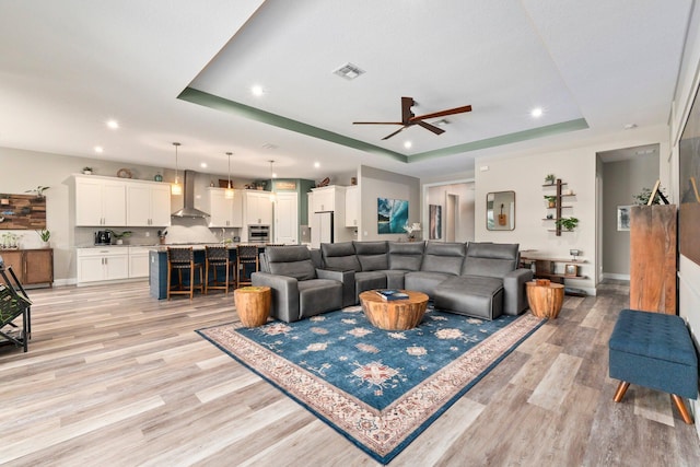 living room featuring light wood-type flooring, a raised ceiling, ceiling fan, and recessed lighting