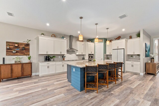 kitchen with freestanding refrigerator, wall chimney exhaust hood, visible vents, and white cabinets