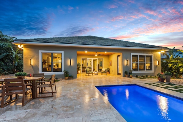 back of property at dusk featuring outdoor dining area, a patio area, stucco siding, and an outdoor pool