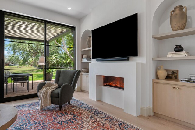 living area featuring built in shelves, light wood-style flooring, and a lit fireplace