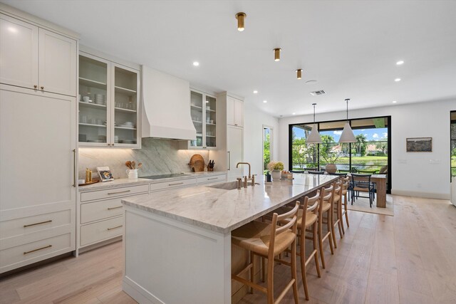 kitchen featuring black electric cooktop, light wood-style flooring, a sink, a large island, and white cabinets