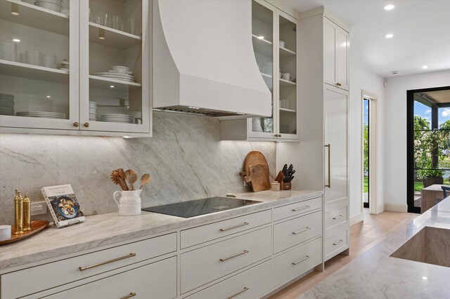 kitchen featuring premium range hood, black electric stovetop, recessed lighting, decorative backsplash, and glass insert cabinets