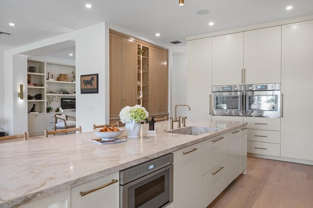 kitchen featuring appliances with stainless steel finishes, a sink, light stone counters, light wood-style floors, and white cabinetry