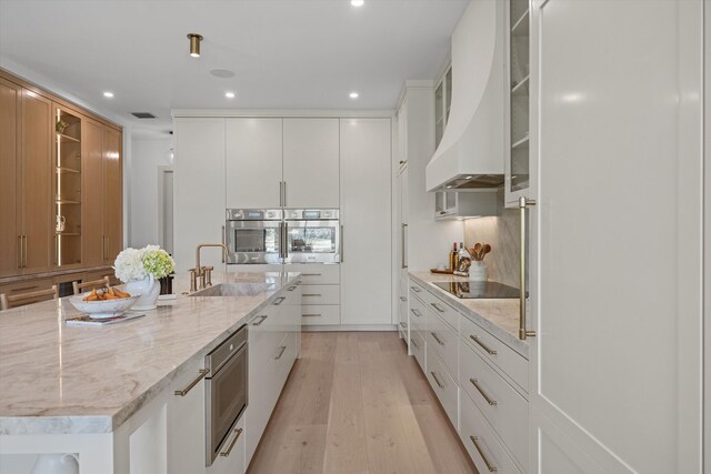 kitchen featuring appliances with stainless steel finishes, a sink, light wood-type flooring, premium range hood, and recessed lighting