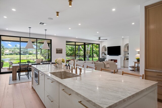 kitchen featuring a sink, a large island with sink, recessed lighting, light wood-style flooring, and white cabinets