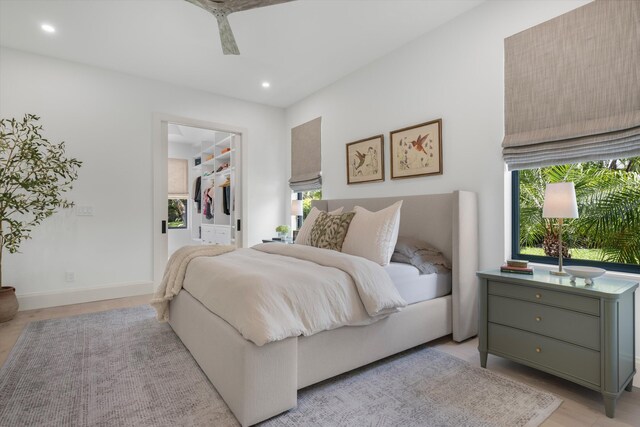 bedroom with a walk in closet, recessed lighting, light wood-style floors, baseboards, and a closet