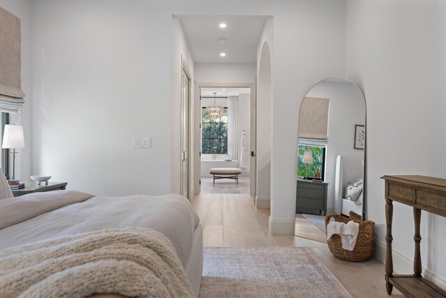 bedroom featuring light wood finished floors, arched walkways, recessed lighting, and baseboards
