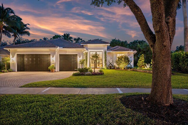 view of front of home with decorative driveway, an attached garage, stucco siding, a lawn, and a tiled roof