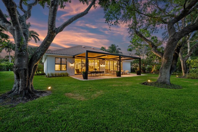 back of house at dusk featuring a patio, a yard, stucco siding, and a tile roof