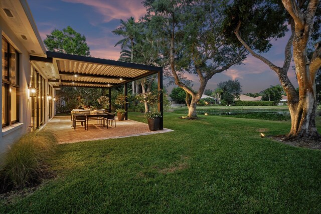 yard at dusk featuring a lawn and a patio